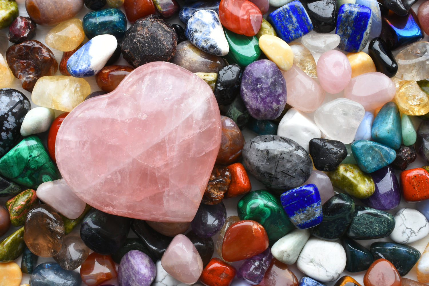 Viele unterschiedliche Halbedelsteine (Heilsteine), mit einem deutlich größeren Rosenquarz in Herzform im Vordergrund